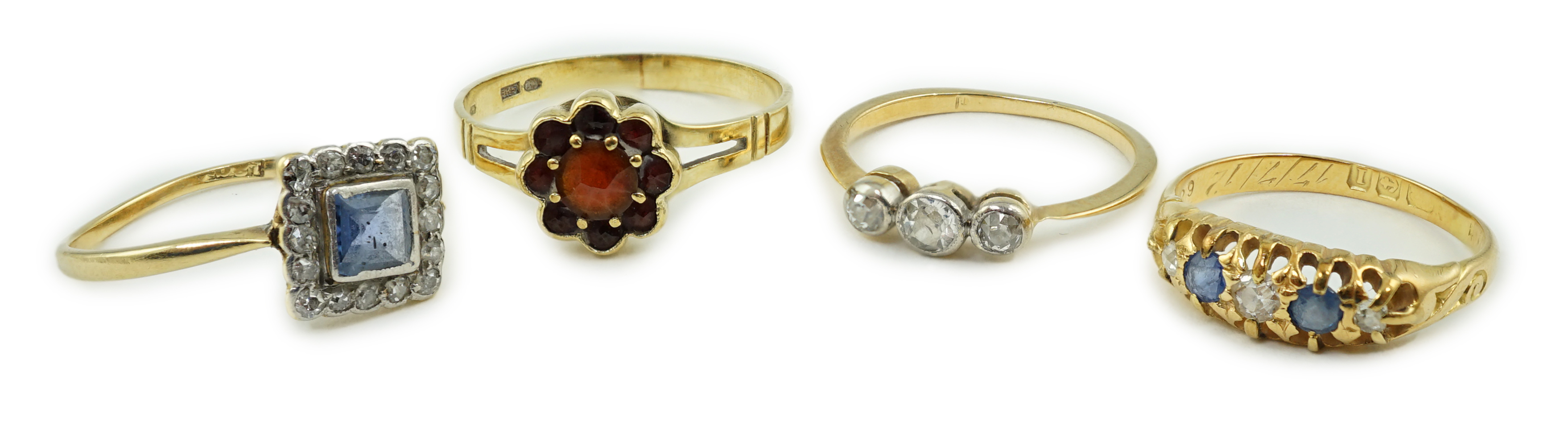 Four assorted rings including an 18ct gold, sapphire and diamond cluster set tablet ring, an 18ct sapphire and diamond half hoop, a gold and three stone diamond and a 14k gold and garnet cluster ring